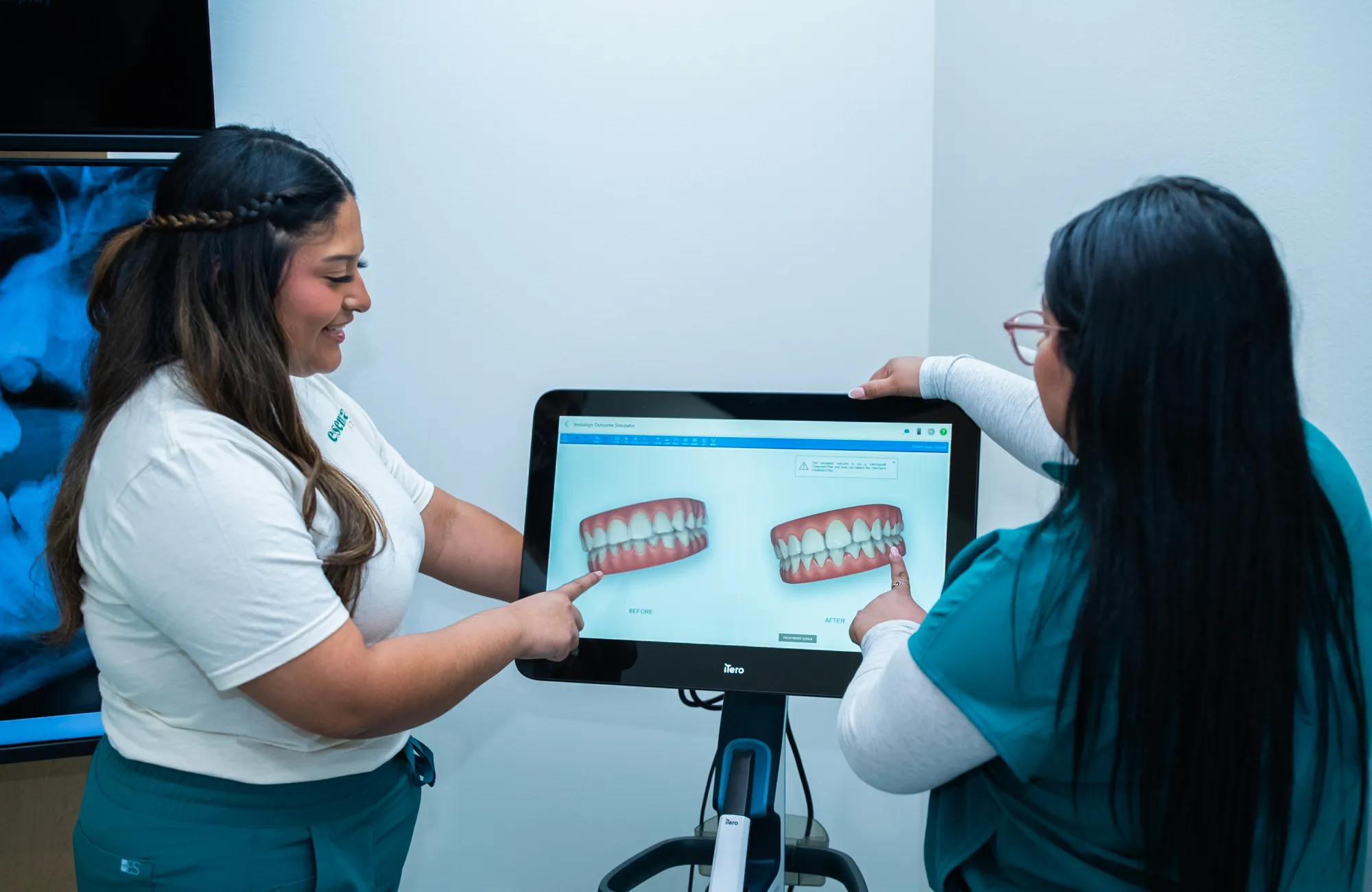 Two women pointing at a dental scan on a monitor, discussing the images.