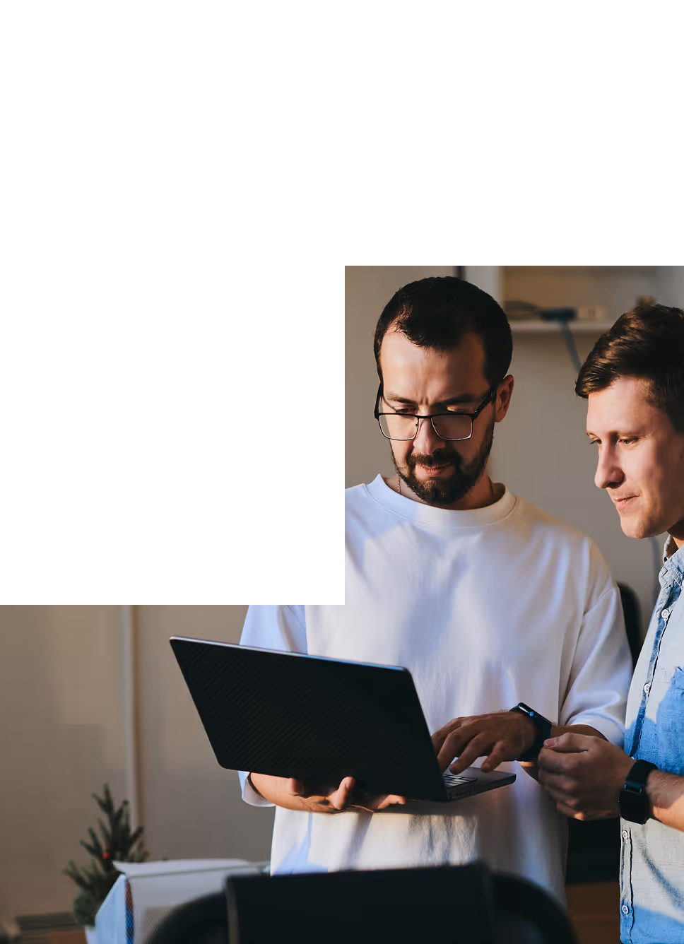 Dwóch mężczyzn pracujących razem, patrząc na laptopa w jasnym pomieszczeniu.