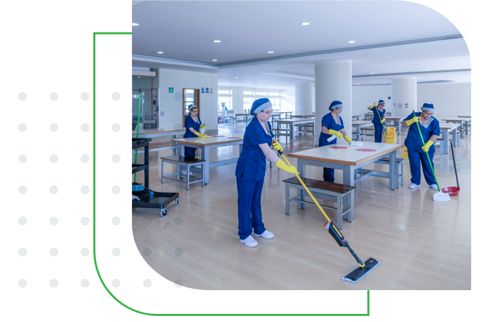 Equipo de aseo con uniforme azul trapeando el suelo y limpiando mesas en un comedor escolar.