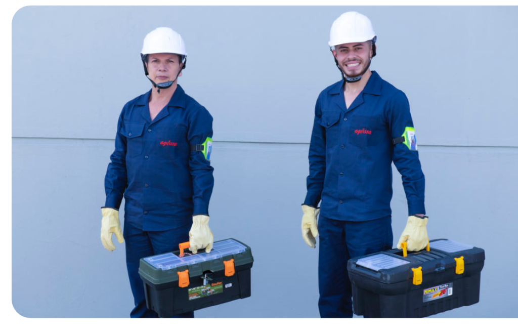 Dos operarios de mantenimiento con uniforme azul, casco y caja de herramientas.
