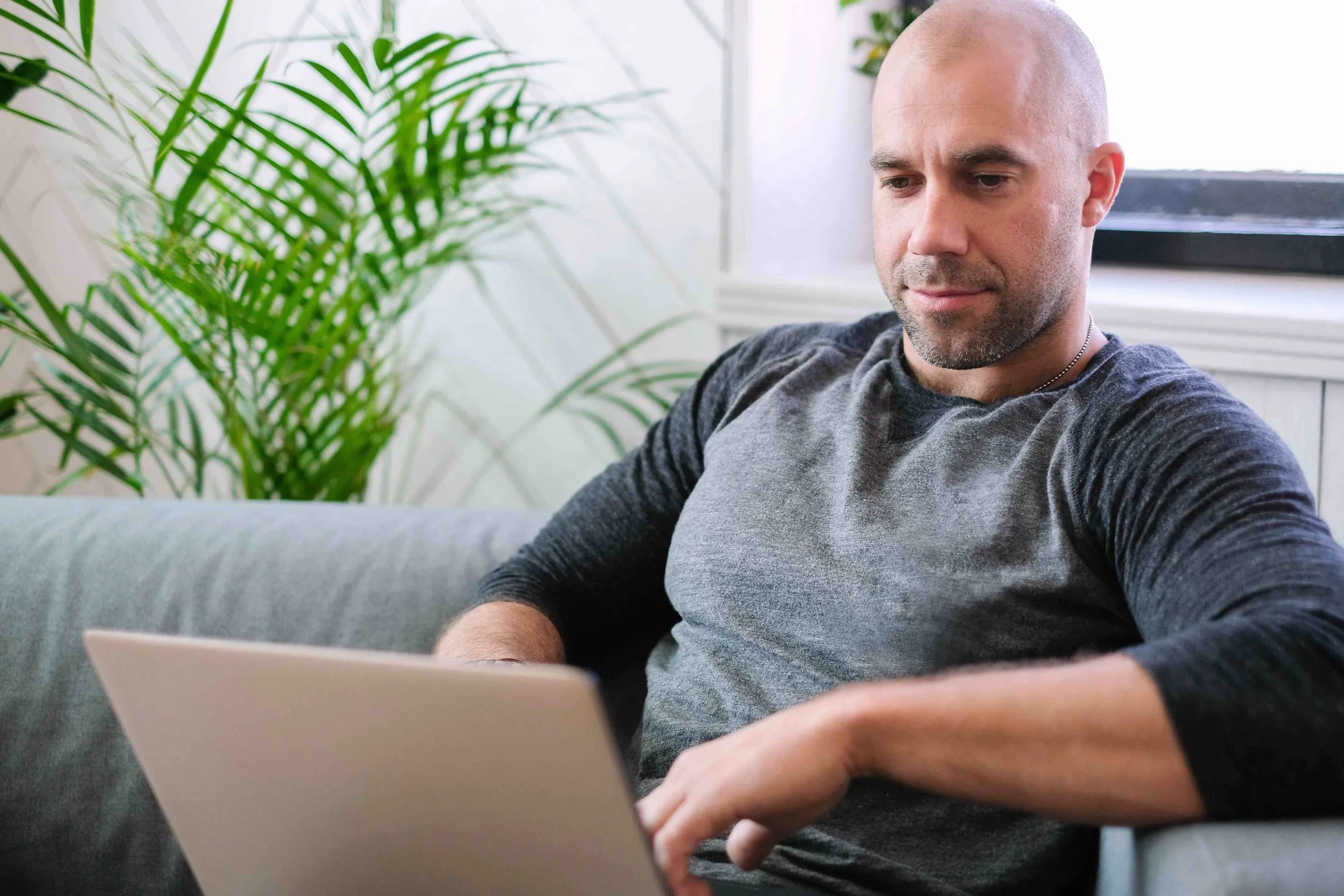 man sitting on a couch using his computer with a neutral expression on his face