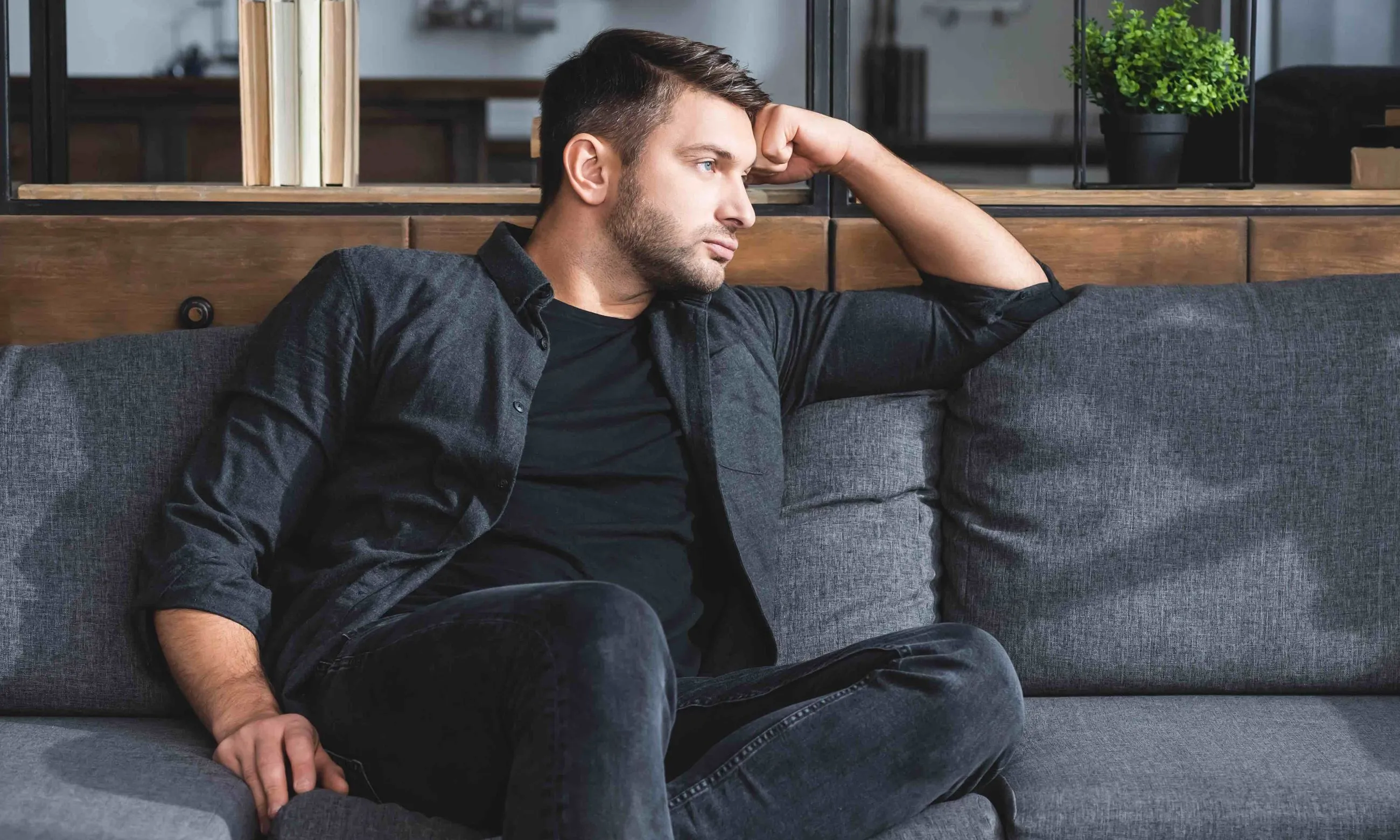 man sitting on a couch looking off to the side thoughtfully