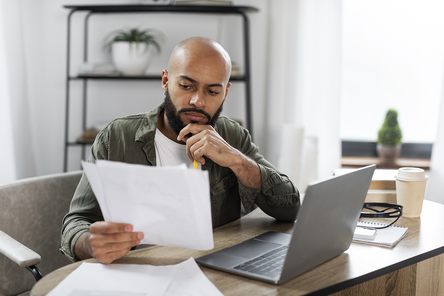 man using laptop and holding paperwork