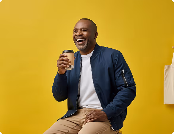 Smiling man sitting in front of a yellow wall holding a coffee cup.