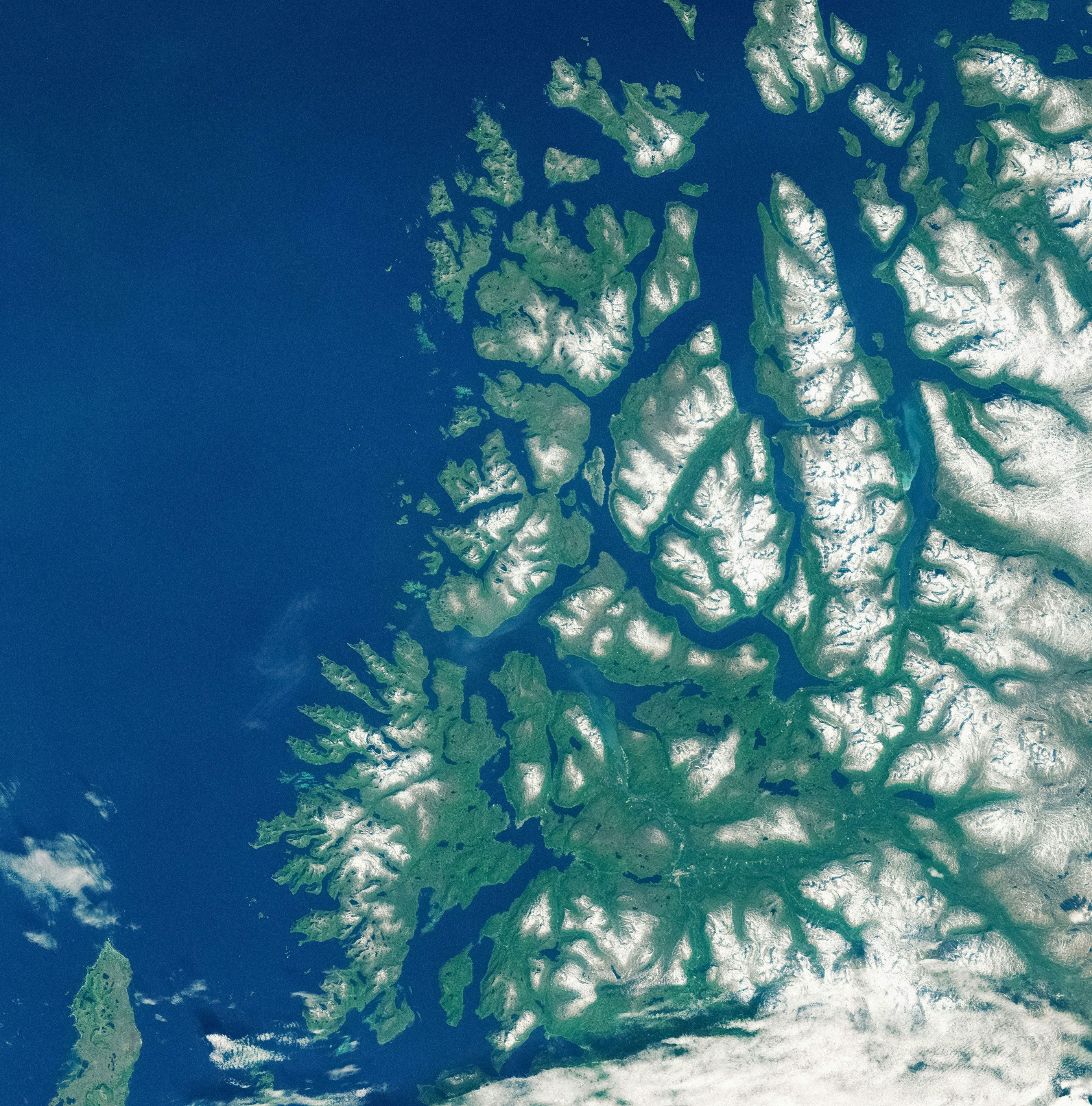 Satellite image of a rugged coastal landscape featuring jagged cliffs, mountainous terrain, and deep blue ocean waters, with high contrast between landforms and sea.