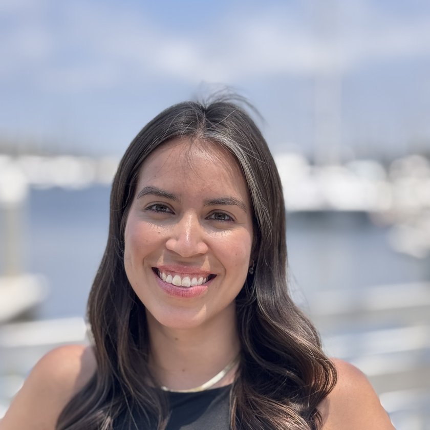 Jay Famiglietti, a man with short gray hair, a neatly trimmed beard, and glasses, smiling in a plaid blazer and collared shirt, standing outdoors with blurred architecture and greenery in the background.