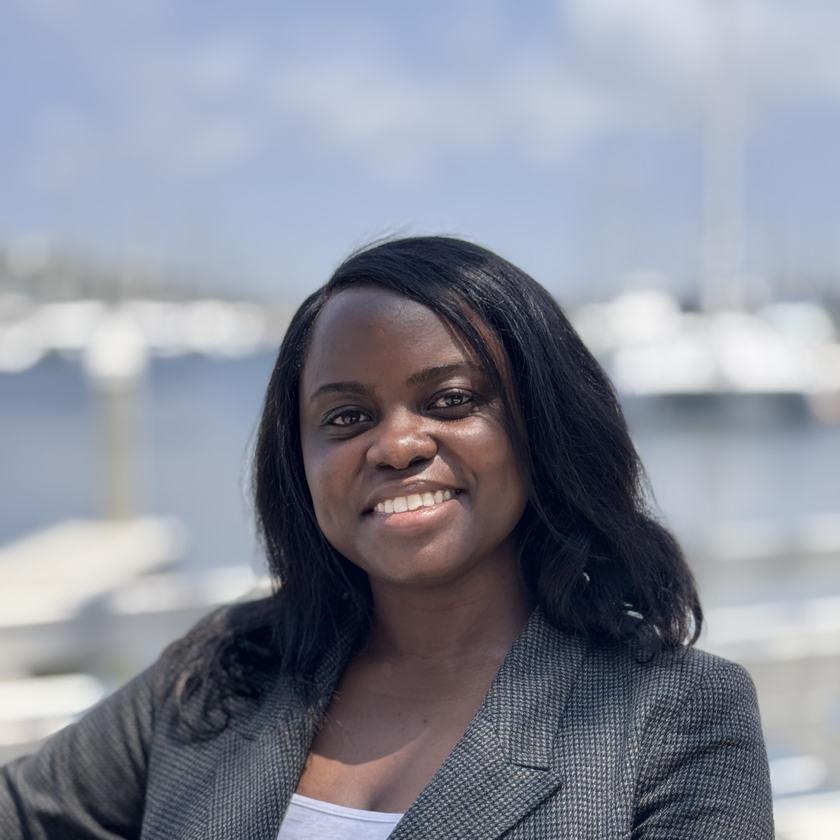 Jay Famiglietti, a man with short gray hair, a neatly trimmed beard, and glasses, smiling in a plaid blazer and collared shirt, standing outdoors with blurred architecture and greenery in the background.