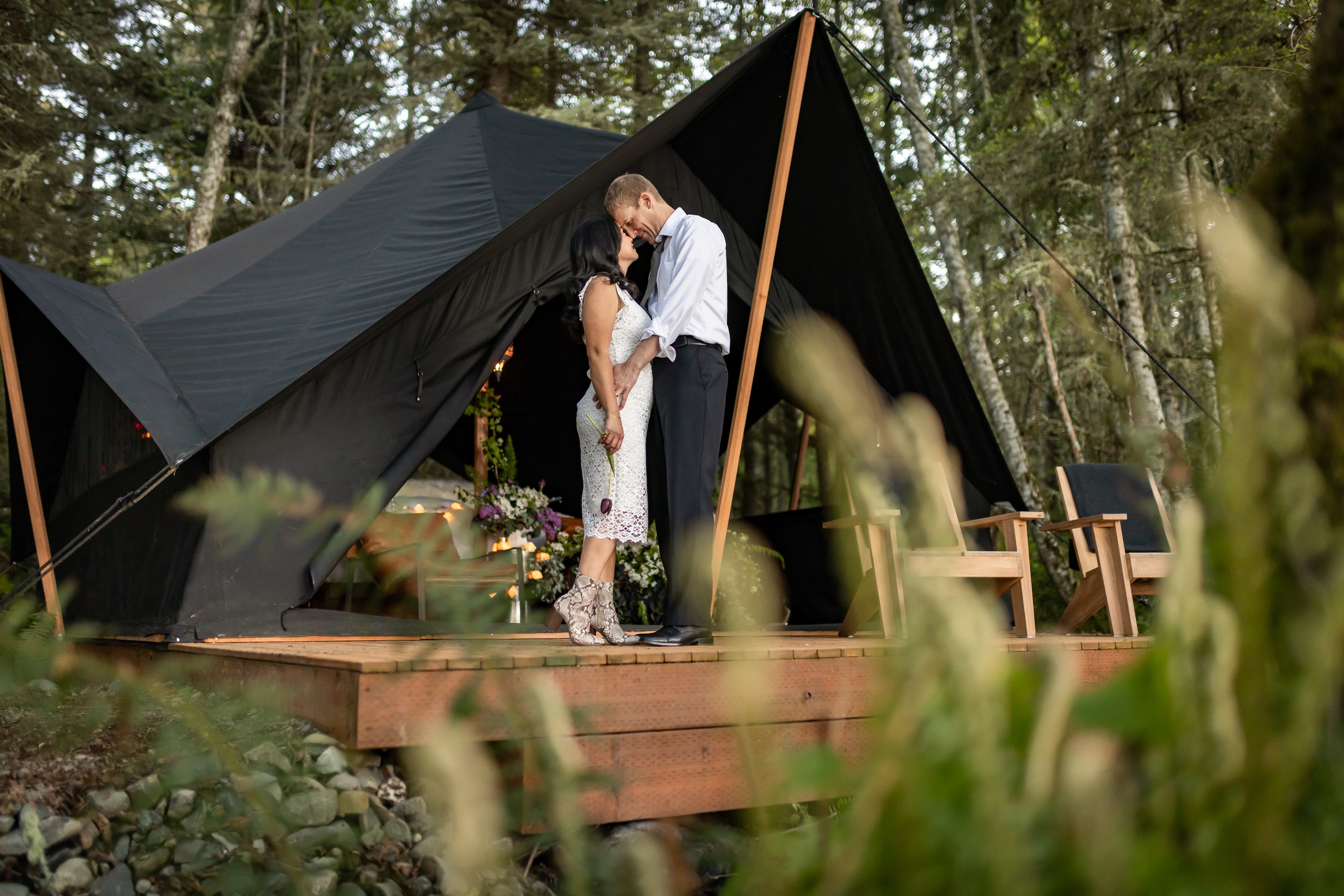 A couple standing together outside their private blackout tent during The Nocturne ritual at Menizei, surrounded by coastal forest.