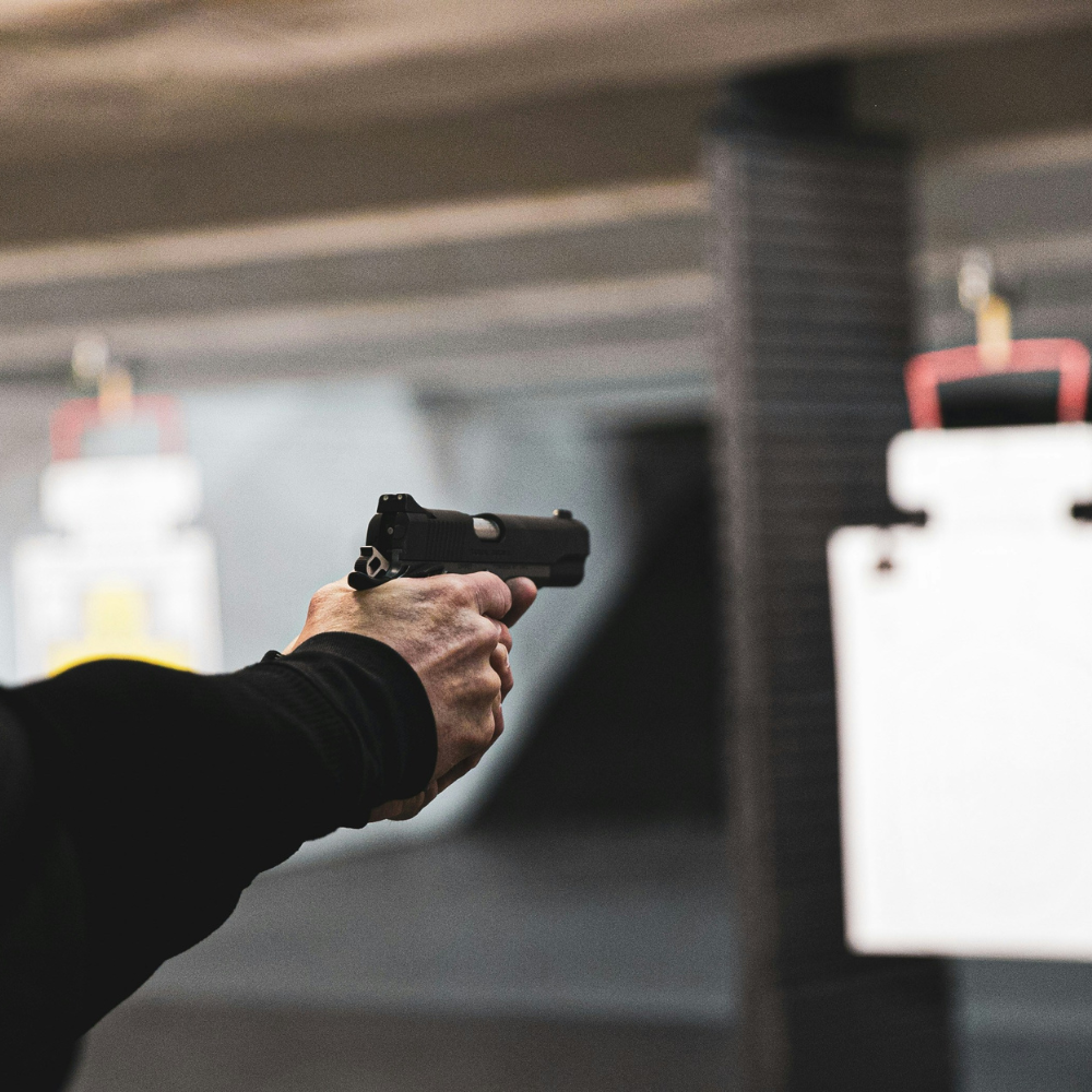 A man wearing ear protection aims a gun at a target in a shooting range setting.