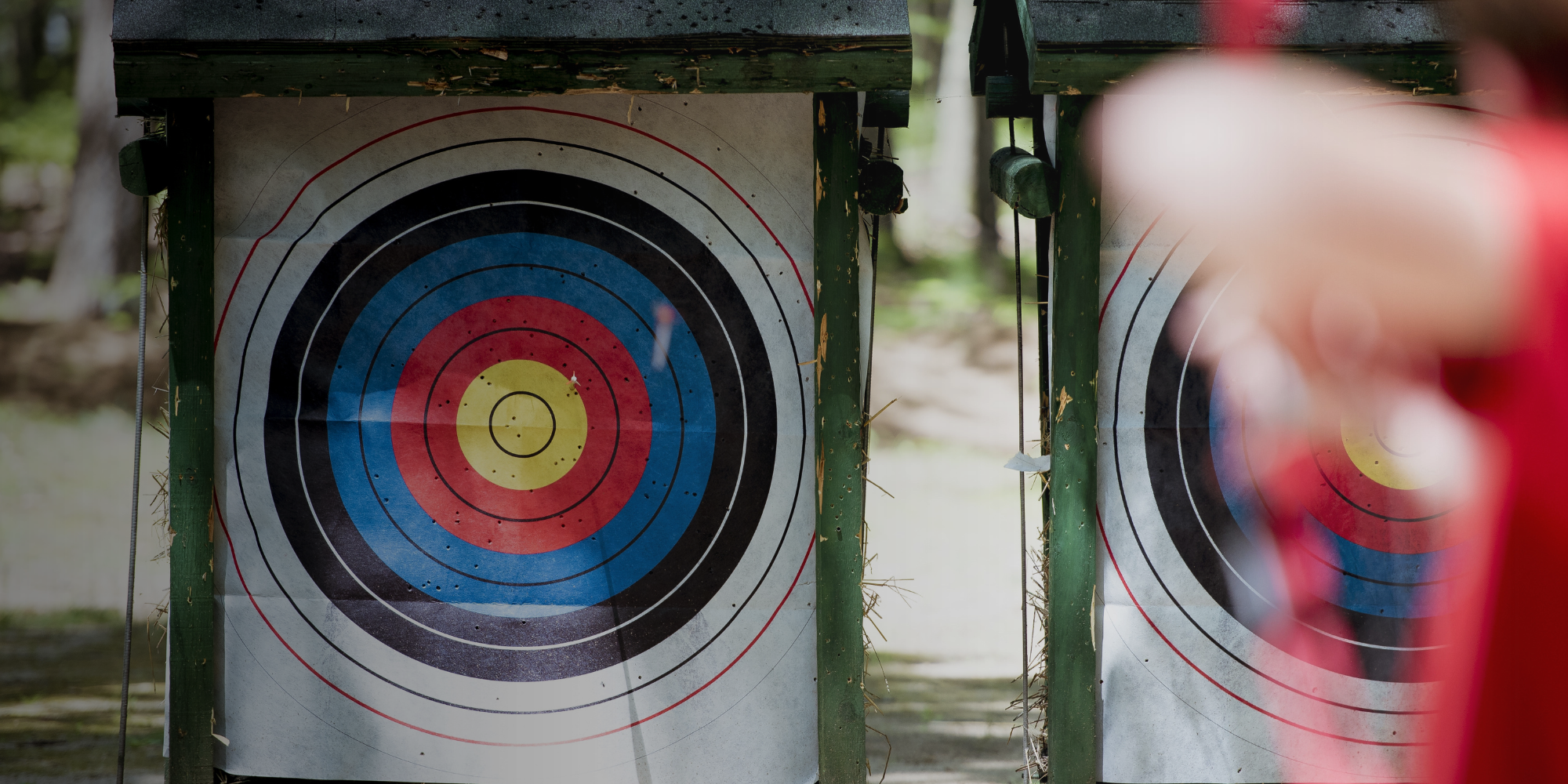 A person aims at a target with a bow, focusing intently on their shot in an outdoor setting.