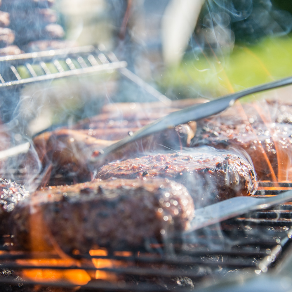 Burgers cooking on a grill outdoors, with smoke rising from the grill.