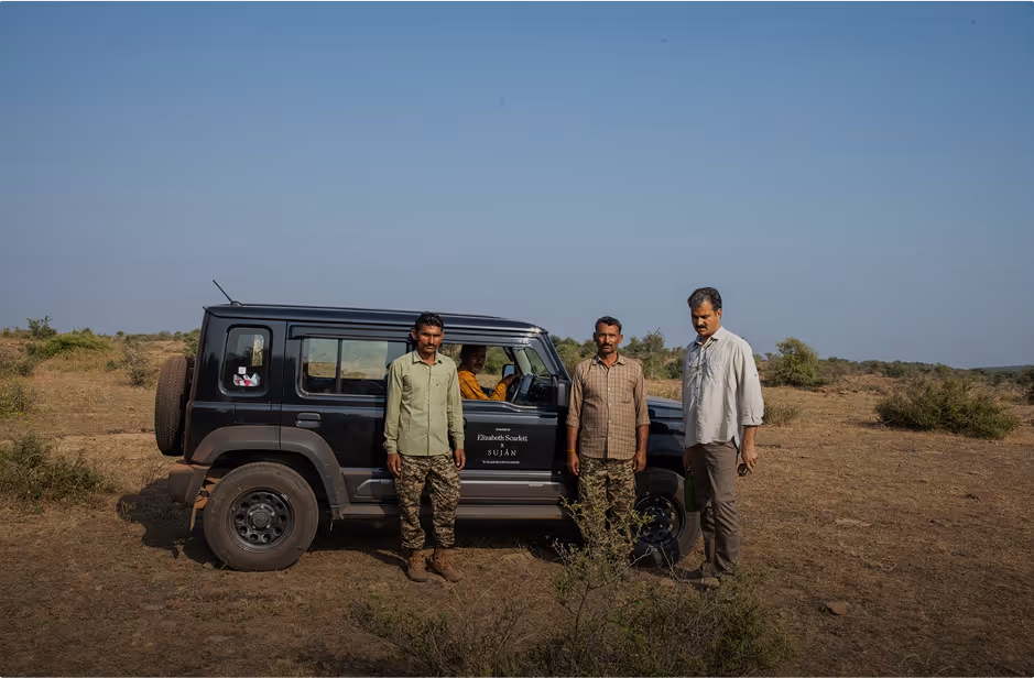 Three men standing beside a black off-road vehicle on a dry, grassy landscape under a clear blue sky.