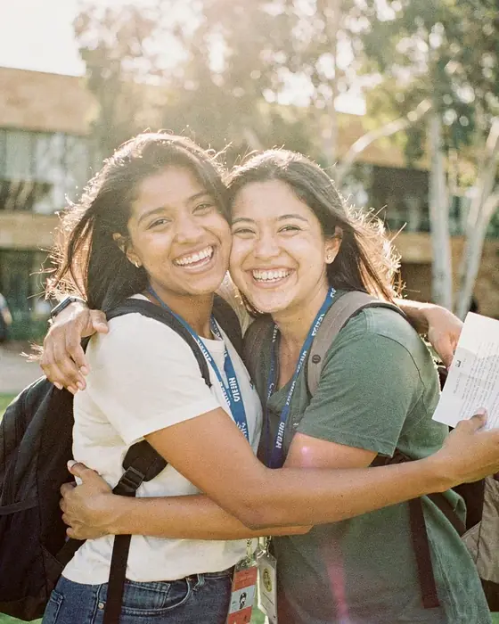 Two students hugging on a university lawn, one holding an offer letter