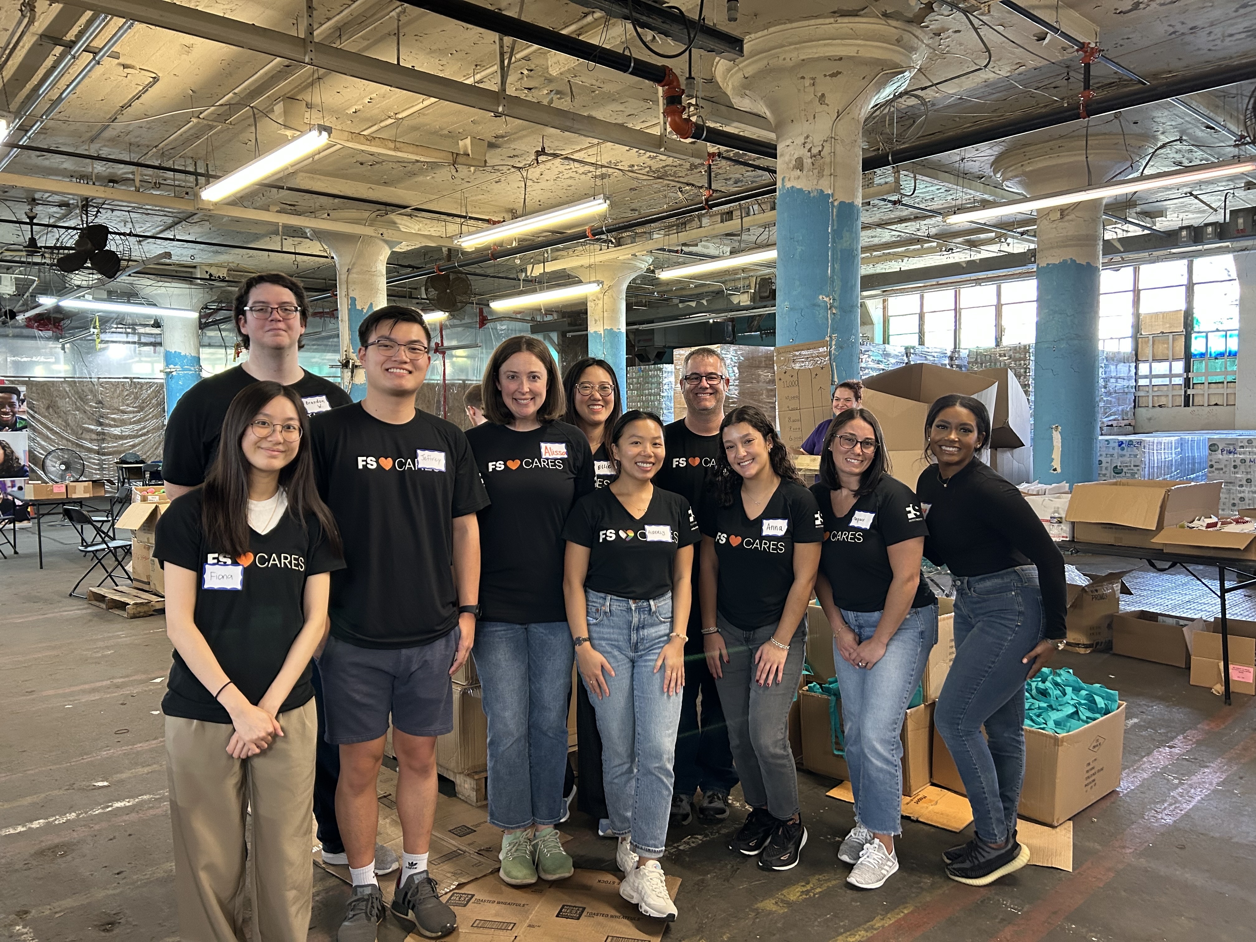 Group photo of volunteers with boxes and materials visible in the background.