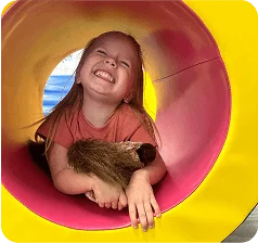 An image of  a girl smiling inside a colorful play tunnel