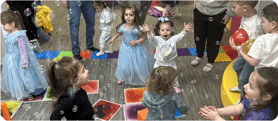 An image of Kids playing with bubbles on colorful mats, some in costumes.