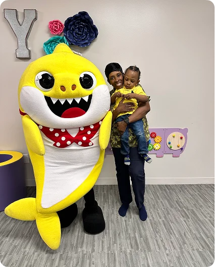  An image of Baby Shark characters posing with happy children in a party setting.