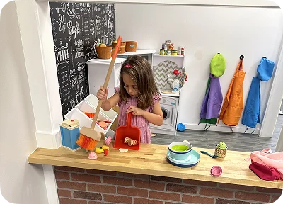 An image of a child playing in a pretend kitchen with toy food and costumes.