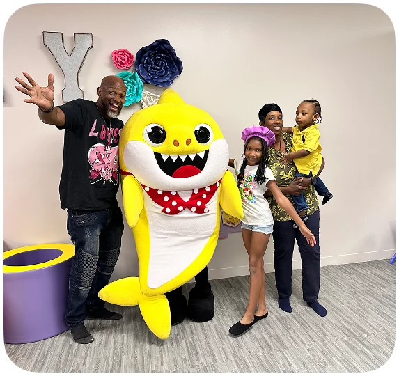 An image of Baby Shark characters posing with happy children in a party setting.