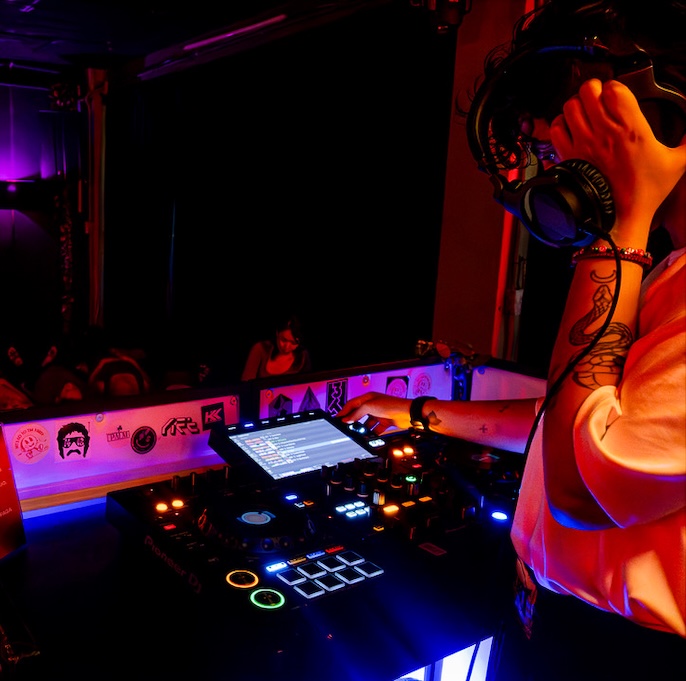 DJ wearing headphones mixing music on a Pioneer DJ controller in a dimly lit club.