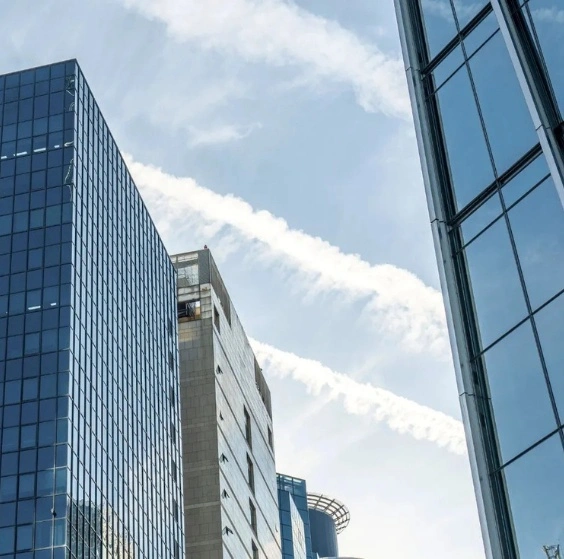 Modern office buildings with glass facades under blue sky and jet trails, reflecting stability, structure, and disciplined investment strategies by a leading investment fund manager in Australia.