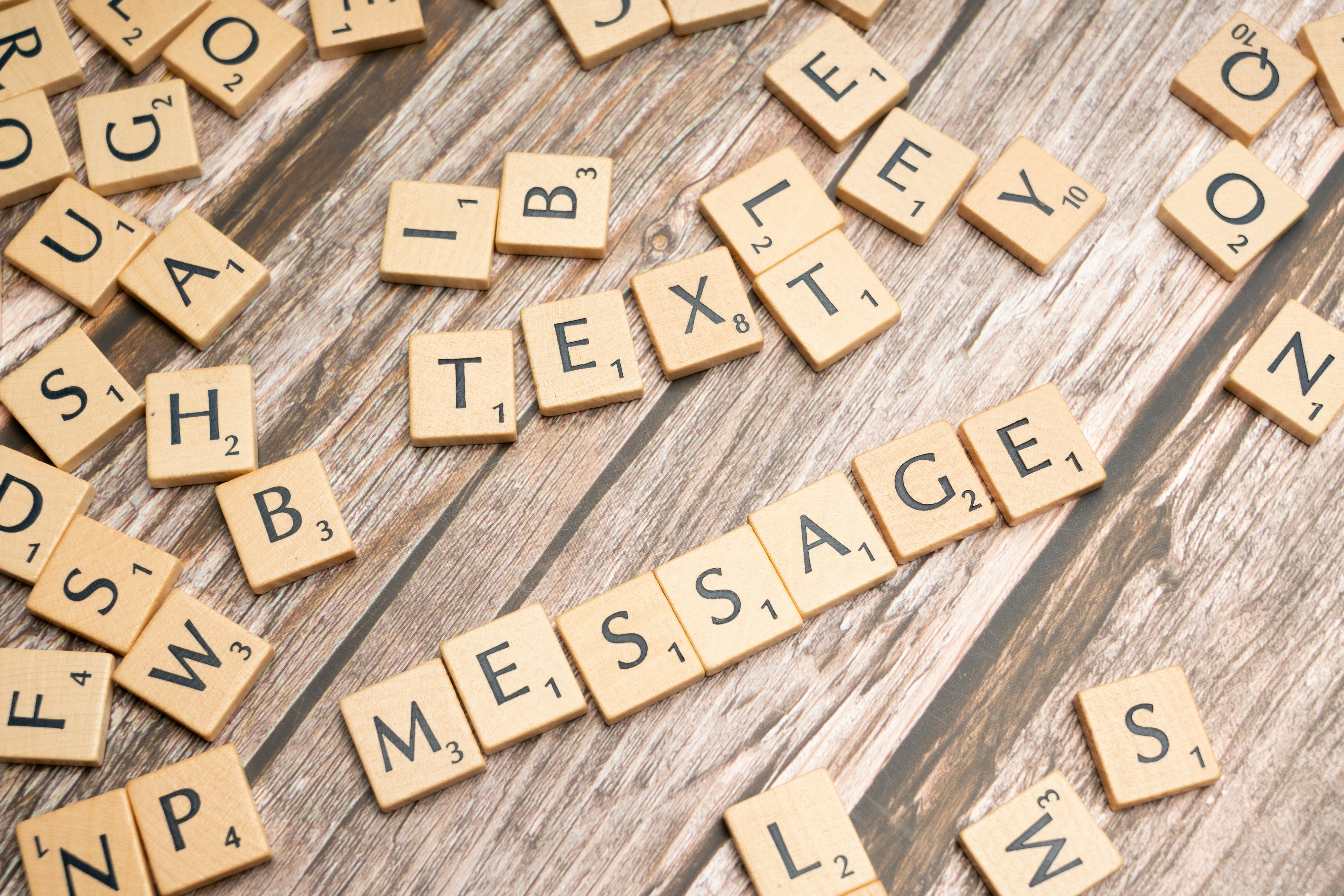 Scrabble tiles layed out randomly on a wooden table with six tiles put toghether in the middle making the word mesage.