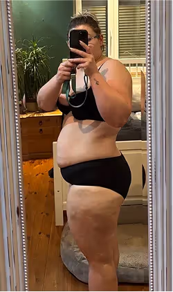 Eine Frau in Sport-BH und Unterwäsche macht ein Selfie im Spiegel.