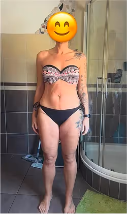Eine Frau im Bikini mit Smiley-Emoji über dem Gesicht steht in einem Badezimmer.