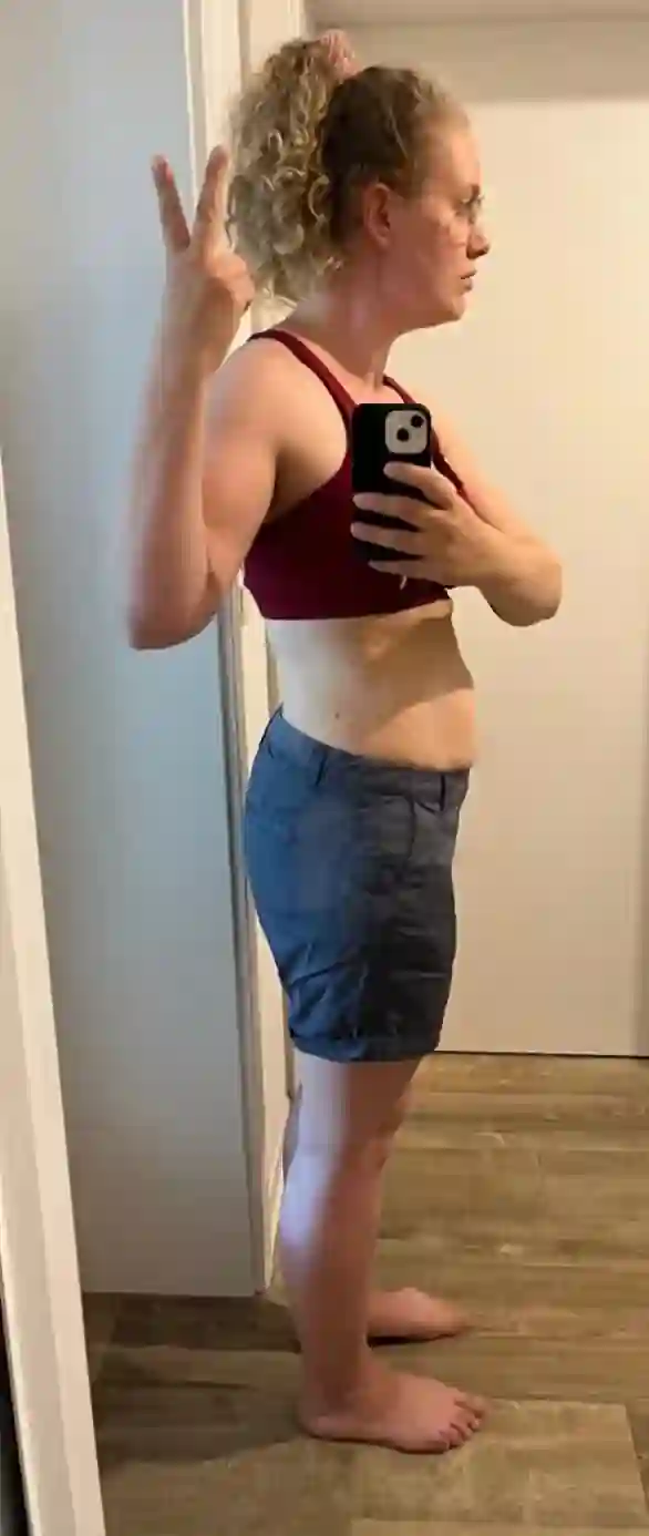 Eine Frau mit lockigen Haaren in Sport-BH und Shorts macht ein Peace-Zeichen und ein Selfie.