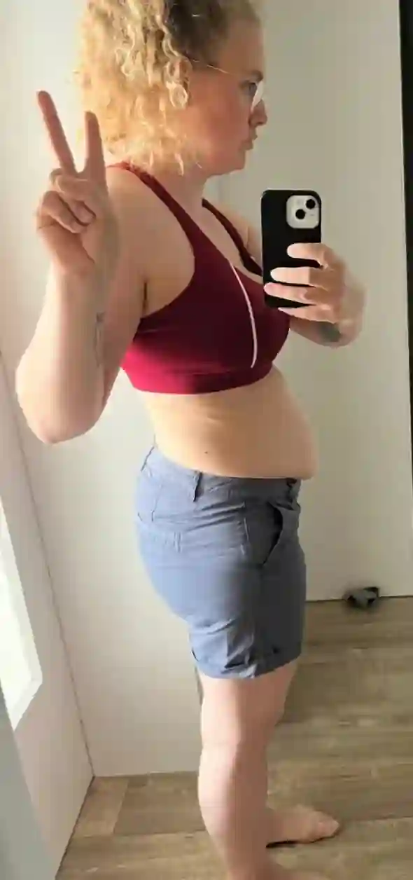 Eine Frau mit lockigen Haaren in Sport-BH und Shorts macht ein Peace-Zeichen und ein Selfie.