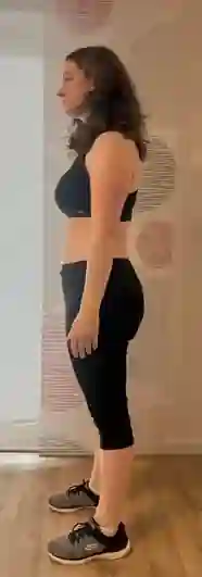 Eine Frau in Sport-BH und Hose steht seitlich.