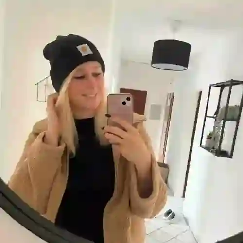 WPF Community - Eine lächelnde Frau mit beiger Jacke und schwarzer Mütze macht ein Selfie im Spiegel.