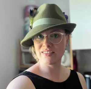 WPF Community - Eine lächelnde Frau mit Brille und einem Hut mit Feder.