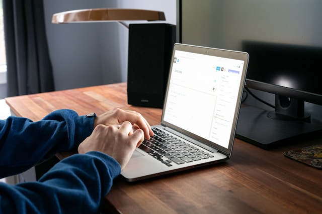Close-up of a person using a MacBook Pro on a brown wooden table to evaluate Shared-Inbox.ai vs. Hiver for team email management.