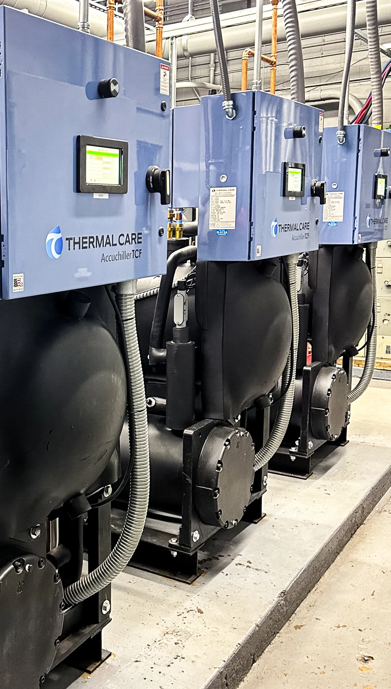 Row of industrial Thermal Care Accuchiller TCF cooling units with blue control panels and black cylindrical bases.
