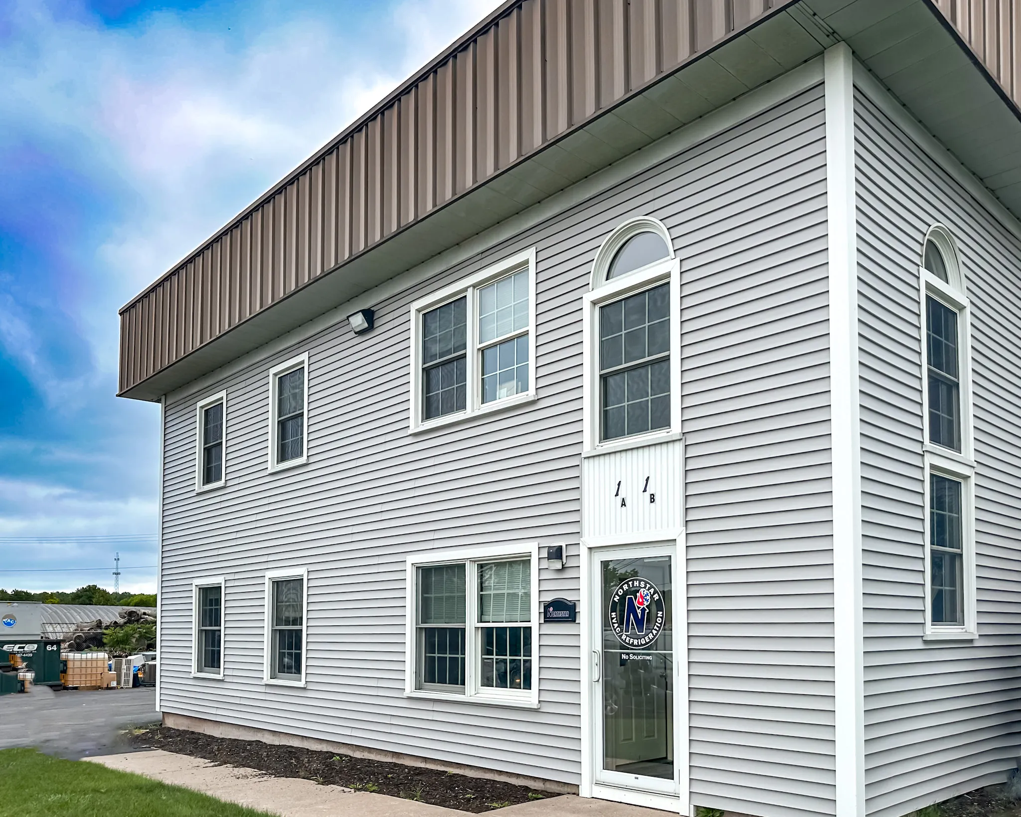 Two-story gray building with white trim and multiple windows under a partly cloudy sky.