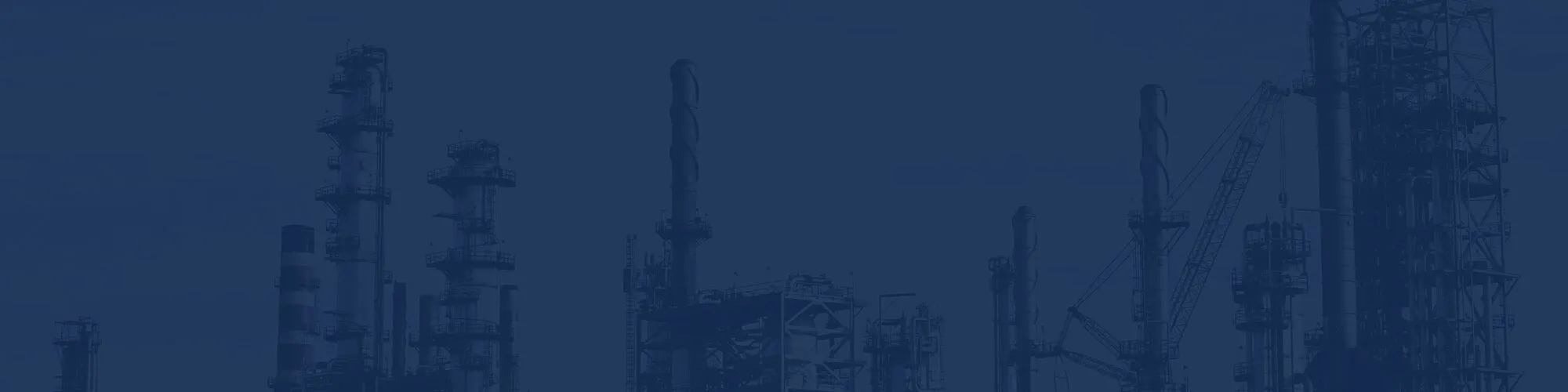 Silhouettes of industrial refinery towers and structures against a dark blue sky.