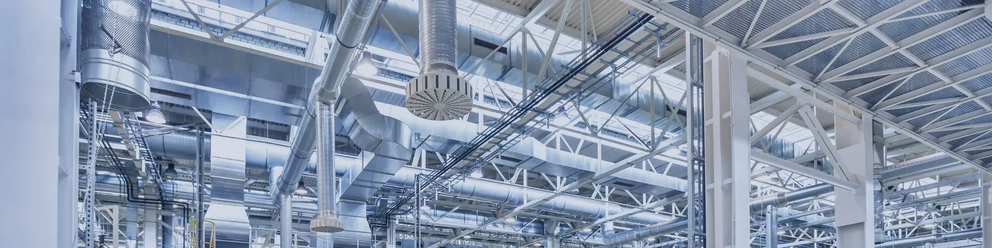 Silver metal air ducts and pipes installed on a high ceiling inside an industrial building.