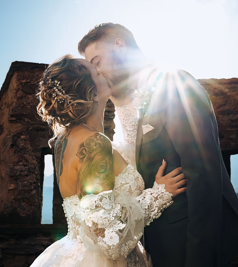 Couple de mariés s'embrassant devant un vieux mur en pierre avec un effet de lumière du soleil éclatant.