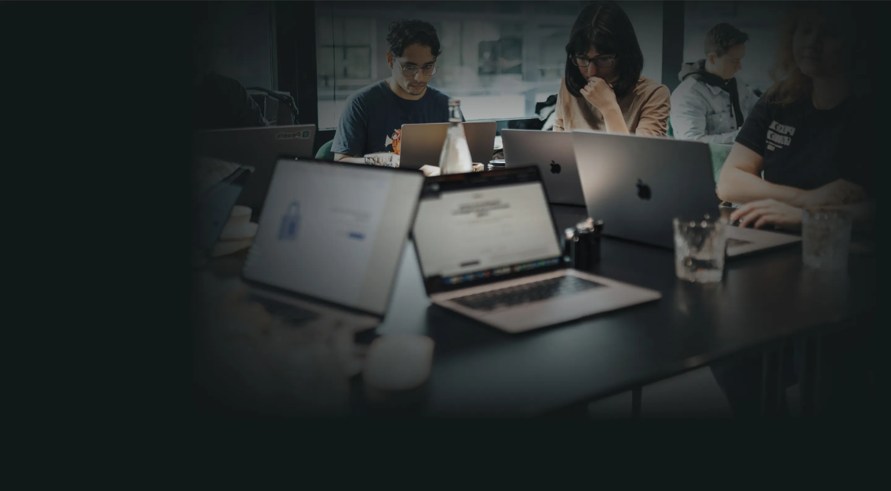 Group of people working on laptops around a table in a modern office.