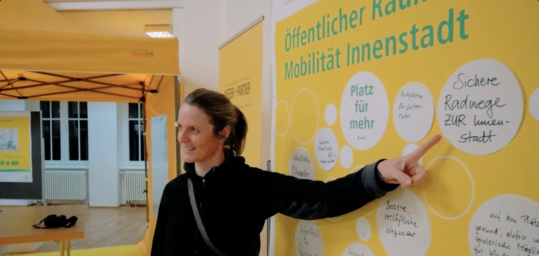 Eine Frau zeigt bei einem Bürgerbeteiligungs-Event in Karlsruhe auf eine gelbe Infotafel zu Plänen für die Innenstadt-Mobilität.