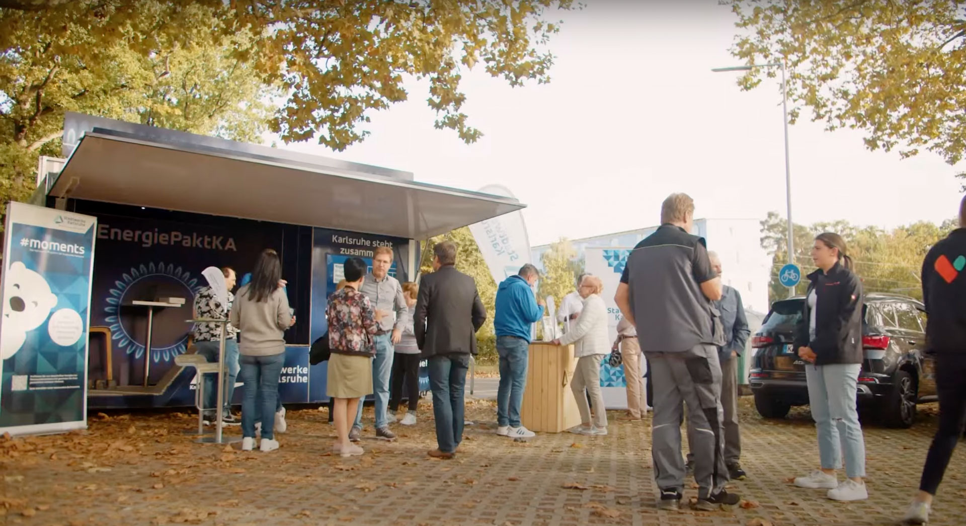Ein lebhaftes Outdoor-Event der Stadtwerke Karlsruhe, bei dem Bürger an einem Informationsstand zu Energiesparthemen beraten werden.