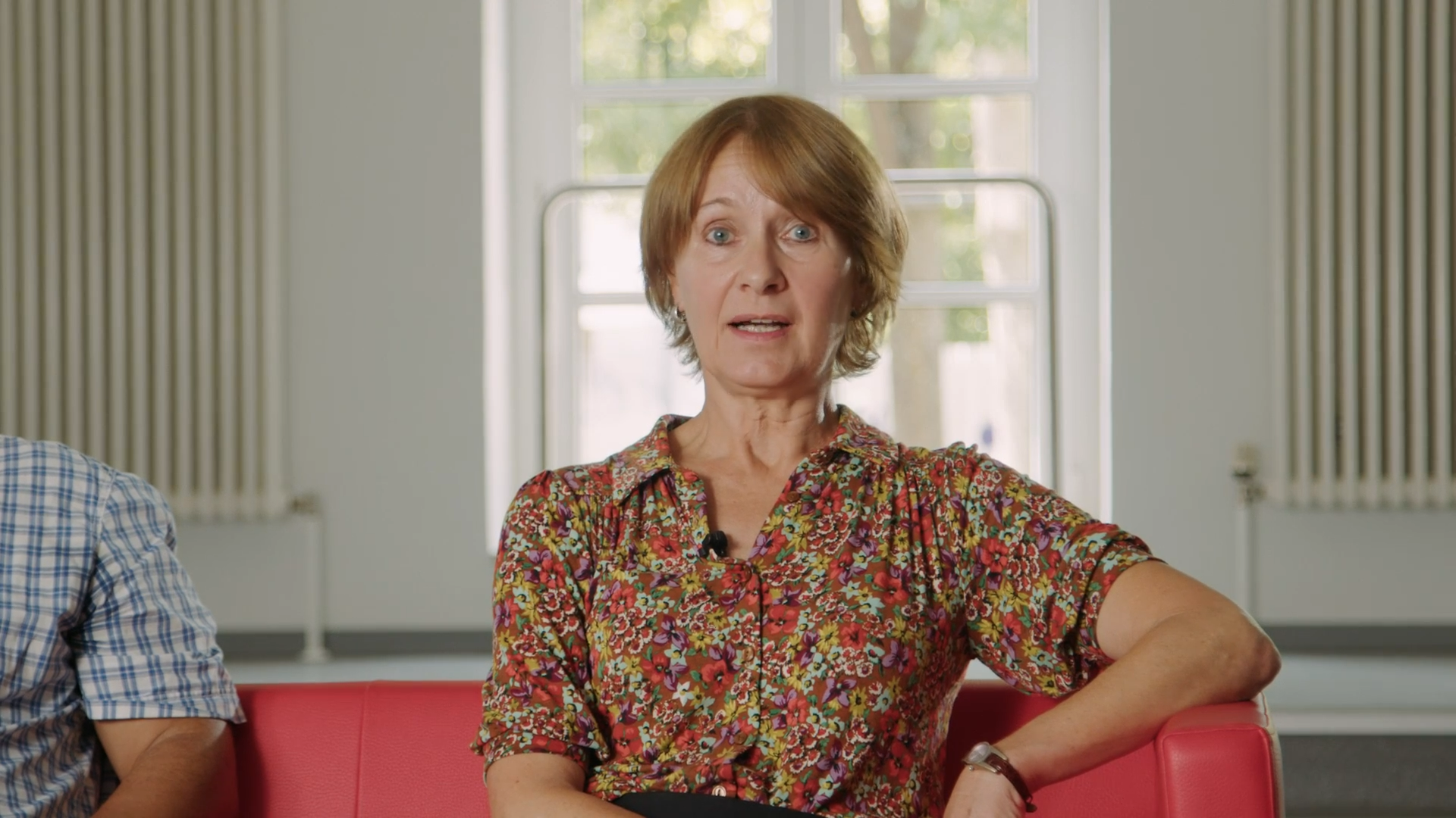 Porträt einer Frau im floralen Hemd auf rotem Sofa, interviewt für den Imagefilm 'Soziale Stadt' Karlsruhe.