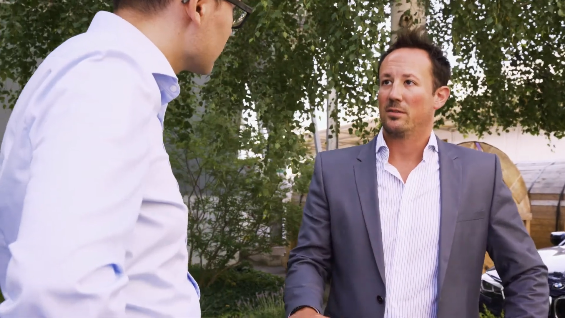 Still der shareBW Videoreihe: Zwei Männer in Businesskleidung im Gespräch unter Bäumen.