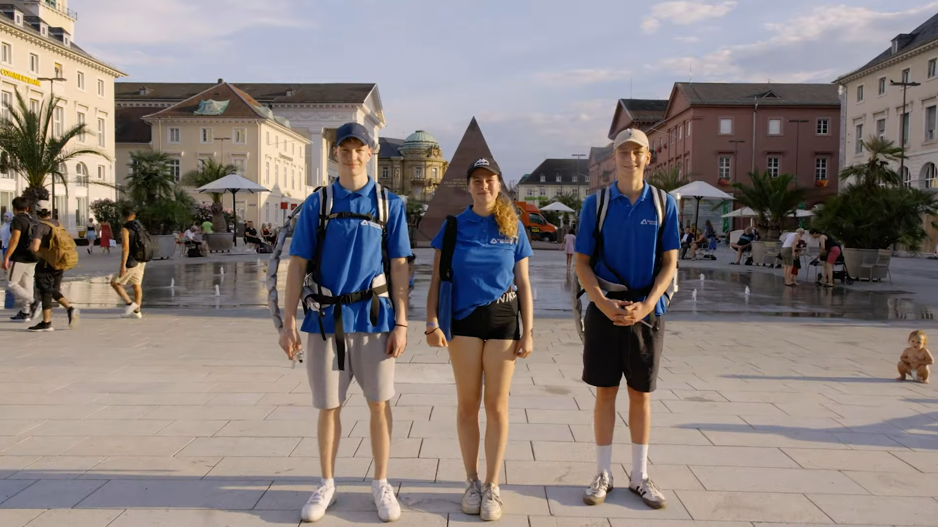 Drei junge Promotoren der Stadtwerke Karlsruhe in blauen Shirts auf dem belebten Schlossplatz mit der Pyramide.