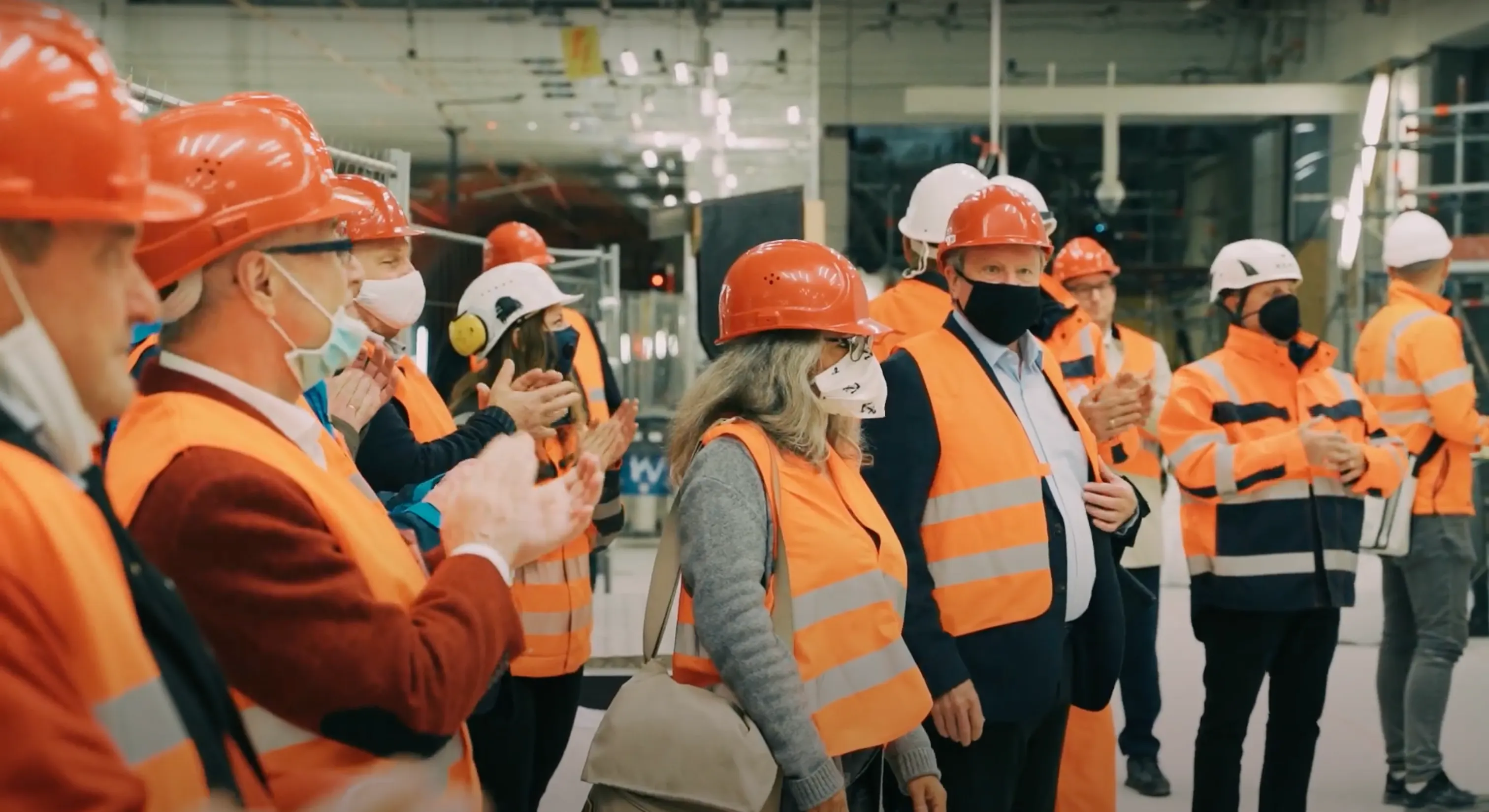 Gruppe in Warnwesten und Bauhelmen in Karlsruher U-Bahn-Station, die Fertigstellung der Lüpertz-Kunstwerke feiernd. Dokumentarischer Stil.