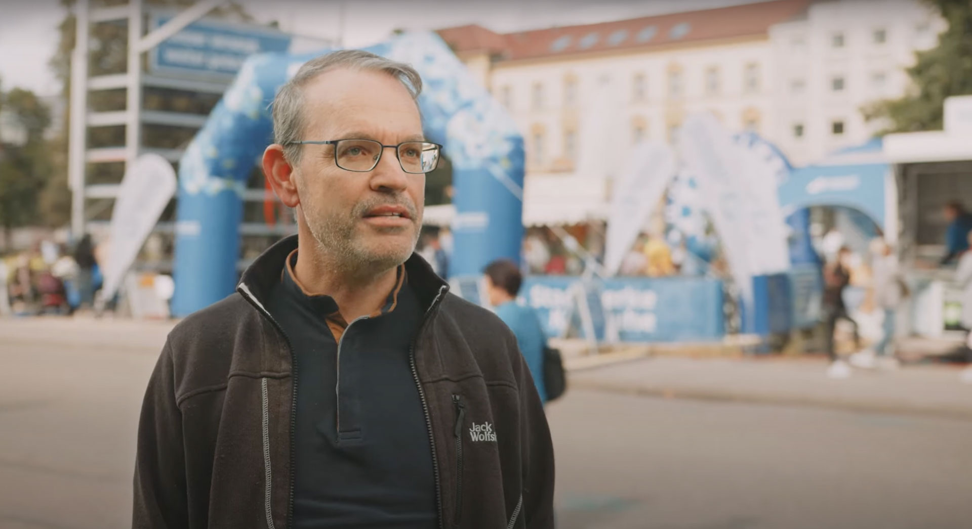Mann mit Brille im Vordergrund, dokumentarische Szene des Stadtwerke Karlsruhe Energiewendetags mit blauen Eventständen und Bögen.