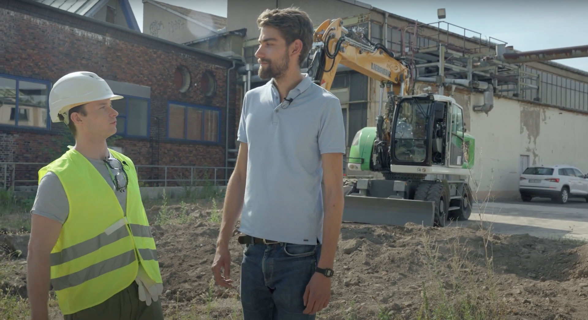 Die Moderatoren des InnoPulsLab-Films auf einer modernen Baustelle mit Bagger im Hintergrund. Visueller Stil eines informativen Erklärfilms zur Baubranche der Zukunft.