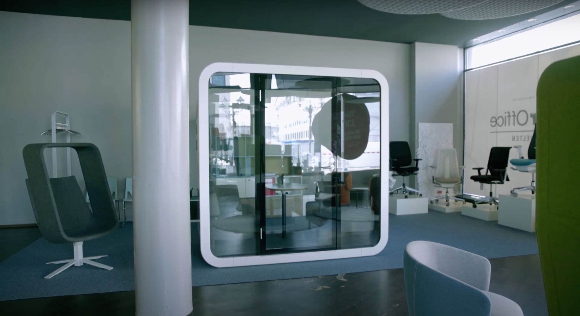Moderne Bürolandschaft mit futuristischer, runder Akustikkabine und ergonomischen Bürostühlen in einem stilvollen Showroom, der New-Work-Konzepte zeigt.