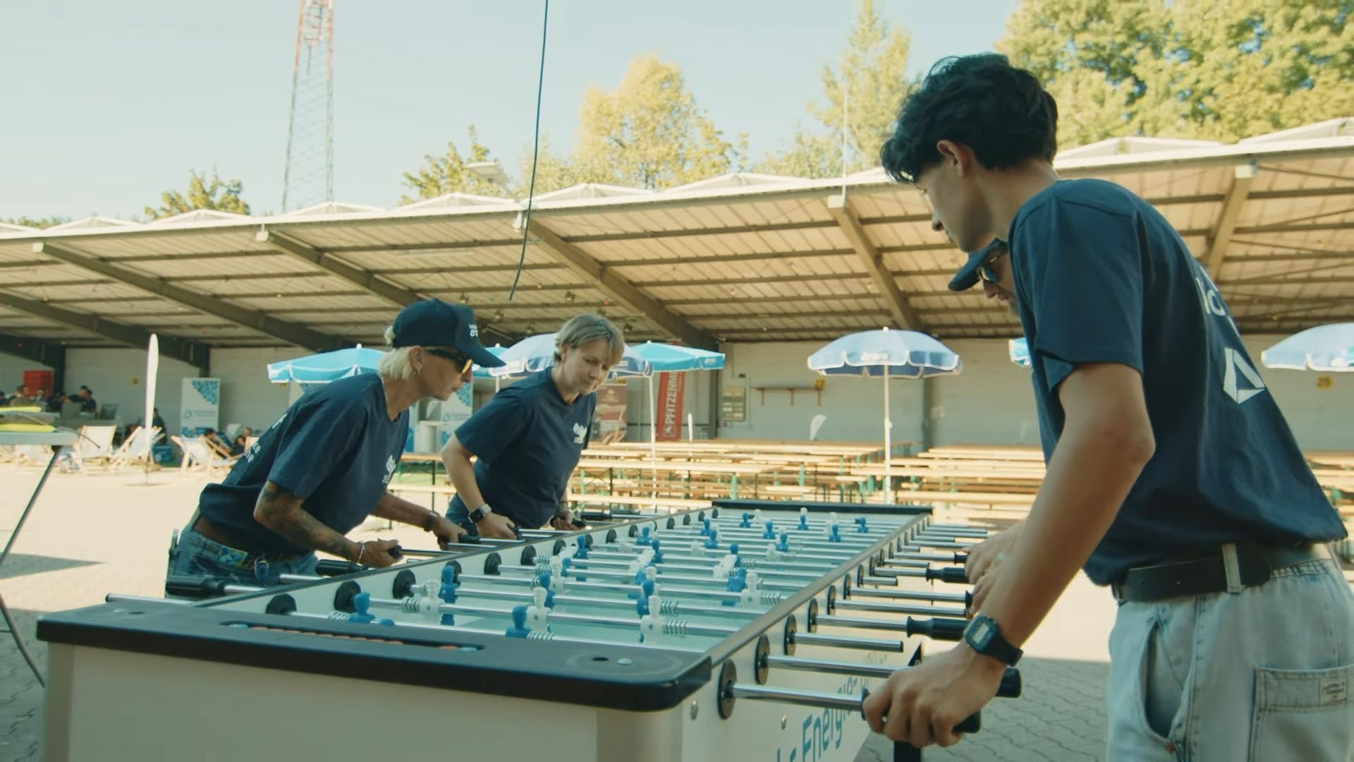Dynamisches Bild dreier Personen beim Kicker-Spiel, das die ungezwungene Gemeinschaft des Stadtwerke Karlsruhe Volkslaufs an einem sonnigen Tag einfängt.